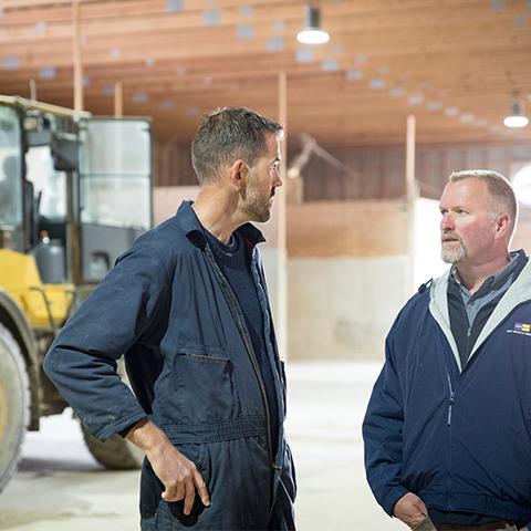 A dairy farmer and dairy cattle nutritionist converse in a feed shed.