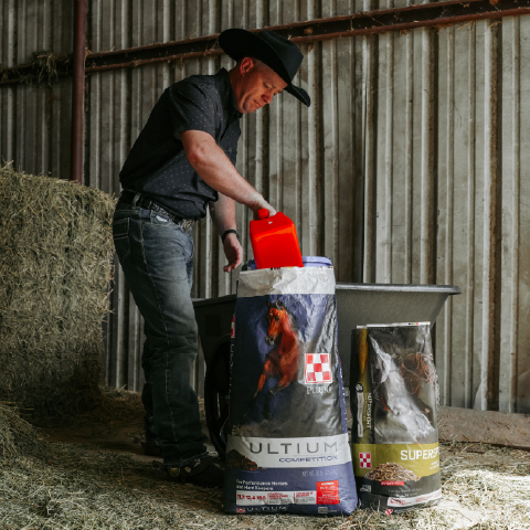 Image of a man using a red feed scoop with a bag of Ultium Feed